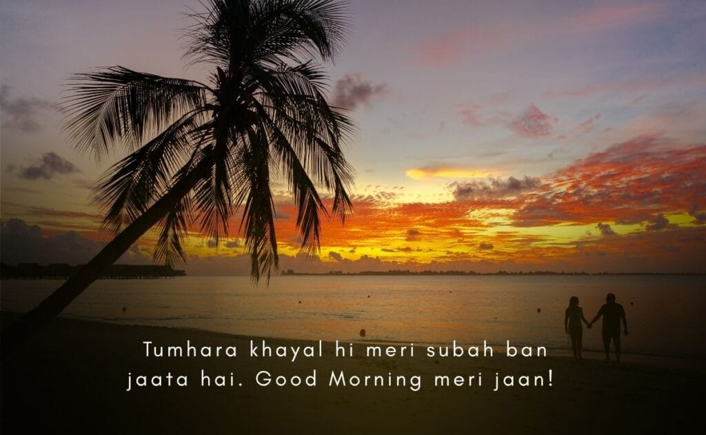 Sunrise over a tranquil beach with a silhouetted couple holding hands by a palm tree. Text reads, “Tumhara khayal hi meri subah ban jaata hai. Good Morning meri jaan!”